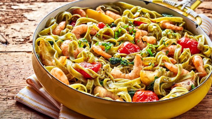 Gourmet seafood Italian tagliatelle pasta with shrimp, tomato, spinach and garlic served on a rustic wooden table in a yellow frying pan, high angle view