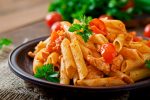 Penne pasta in tomato sauce with chicken, tomatoes on a wooden background