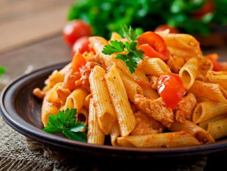 Penne pasta in tomato sauce with chicken, tomatoes on a wooden background