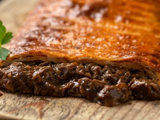 Steak and onion lattice pie on rustic wooden board.