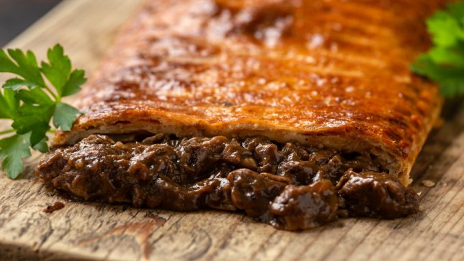 Steak and onion lattice pie on rustic wooden board.