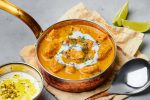 Murgh Makhani or Butter Chicken in copper bowl on gray concrete table top. Indian Cuisine dish with chicken meat and creamy masala. Asian food and meal. Close up
