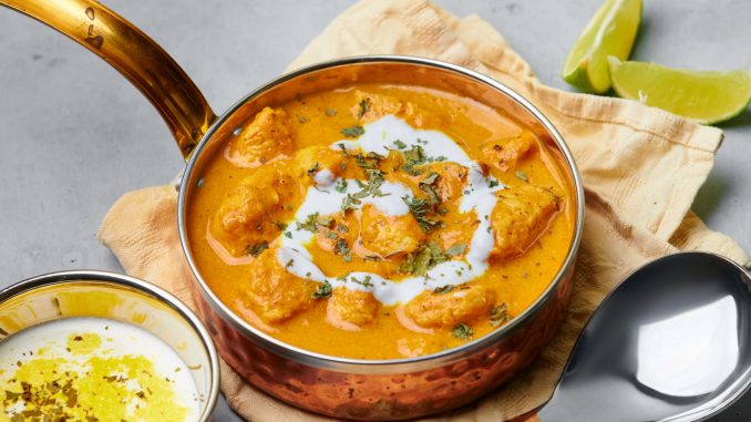 Murgh Makhani or Butter Chicken in copper bowl on gray concrete table top. Indian Cuisine dish with chicken meat and creamy masala. Asian food and meal. Close up