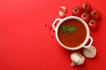 Bowl with tomato soup and ingredients on red background.