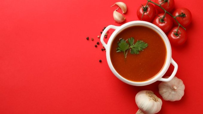 Bowl with tomato soup and ingredients on red background.