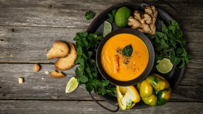 Fresh homemade cream of carrot soup with baked peppers, carrots and cheese, lime juice and ginger, served with nuts and fresh mint, place for text, top view.