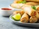 Fried spring rolls with sweet chili sauce and lime on plate.