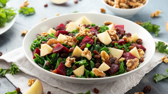 Kale salad with apple, beetroot, walnut and raisins in white plate. Healthy food