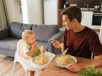 Upper view of dad and baby in high chair eating spaghetti for lunch at kitchen table. Safety assessments are needed for all novel foods.