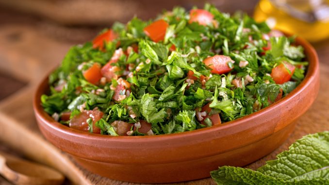 A bowl of delicious fresh tabouli with parsley, mint, tomato, onion, olive oil, lemon juice, and bulgar wheat.