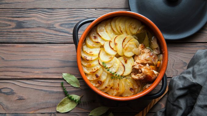 Homemade Lancashire hotpot on wooden background - a stew consists of lamb, onion, carrot, Worcestershire sauce, topped with sliced potatoes, bay leaves, thyme and baked in a heavy pot on a low heat