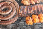 A close up view of beef spare ribs, sausage and chicken cooking on a open braai or barbecue on a warm summers day