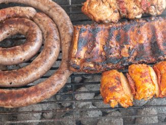 A close up view of beef spare ribs, sausage and chicken cooking on a open braai or barbecue on a warm summers day