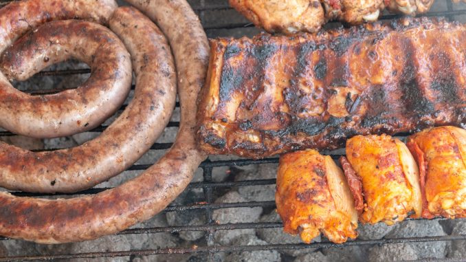A close up view of beef spare ribs, sausage and chicken cooking on a open braai or barbecue on a warm summers day