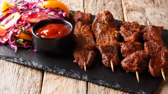 Nigerian barbecue: suya on skewers with fresh vegetable salad and ketchup close-up on the table. horizontal
