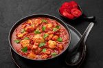Chicken Madras Curry in black bowl on dark slate table top. Indian cuisine dish with with chicken meat and spicy masala gravy. Asian food and meal.
