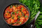 Chicken Vindaloo with spinach in black bowl on dark slate table top. Indian cuisine meat chilli curry dish. Authentic asian food.