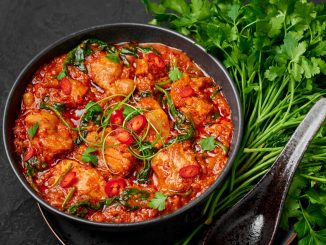 Chicken Vindaloo with spinach in black bowl on dark slate table top. Indian cuisine meat chilli curry dish. Authentic asian food.