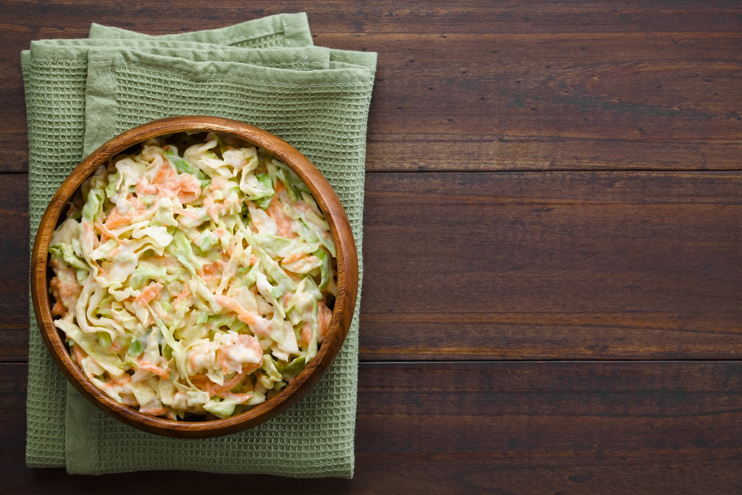 Coleslaw made of freshly shredded white cabbage and grated carrot with homemade mayonnaise-based salad dressing in wooden bowl, photographed overhead with copy space on the right side (Selective Focus, Focus on the salad)