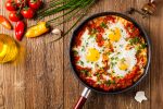 Shakshouka, dish of eggs poached in a sauce of tomatoes, chili peppers, onions. Top view.