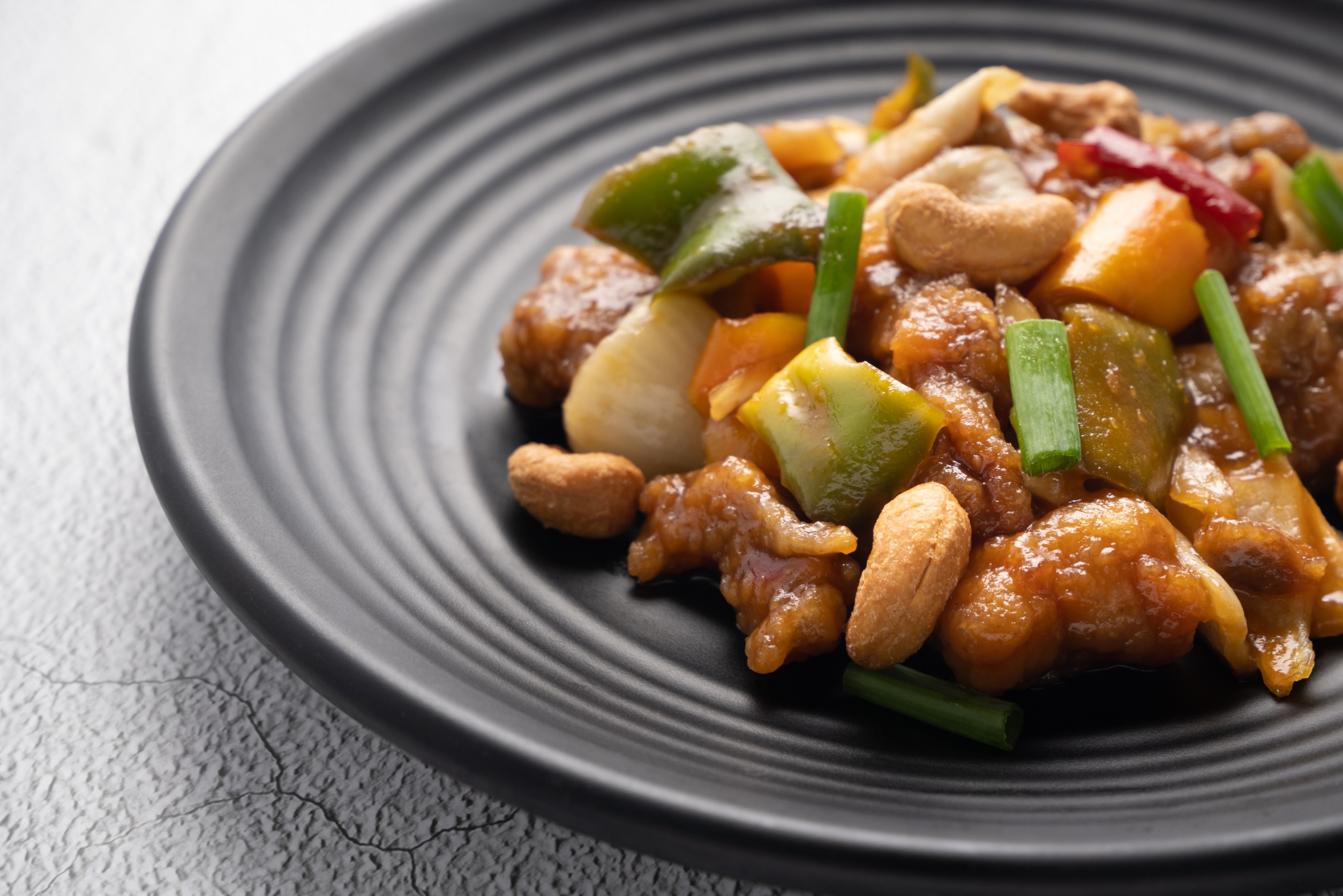 Stir fried chicken with cashew nuts in black dish on concrete table.