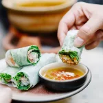 Hand dipping Vietnamese spring roll in sauce