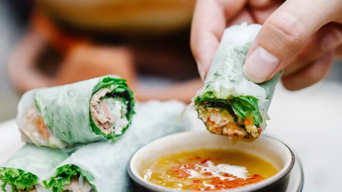 Hand dipping Vietnamese spring roll in sauce