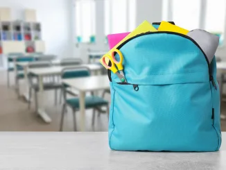 back to school, satchel on table. Light blue backpack with stationery on school desk in classroom. Space for text