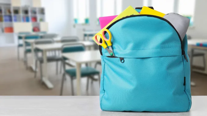 back to school, satchel on table. Light blue backpack with stationery on school desk in classroom. Space for text