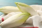 Fresh raw Belgian endives (chicory) on light blue table, closeup. The basis of chicons gratin.