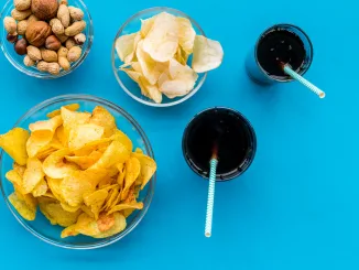 Snacks for TV watching. Chips, nuts, soda, rusks on blue background top view. Are UPFs the enemy?