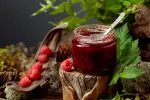 A jar of raspberry jam with fresh berries on an old tree trunk in the forest. A concept of healthy, eco-friendly food.
