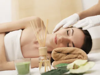 Beautiful young woman getting facial massage lying on the couch. Top view focused on the face