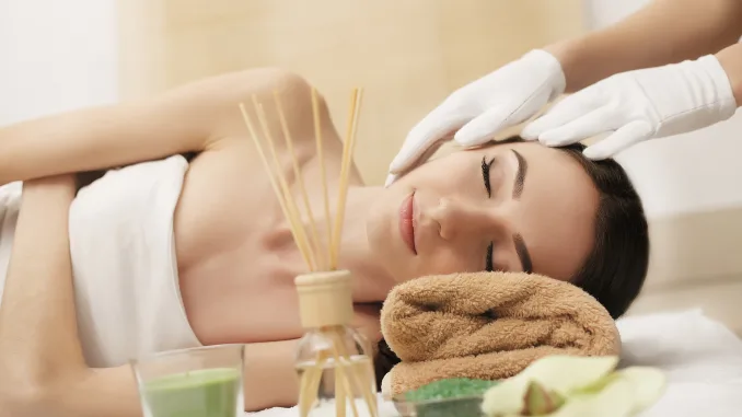 Beautiful young woman getting facial massage lying on the couch. Top view focused on the face