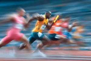 Athletes sprint energetically in a relay race, focusing on a smooth baton handoff while competing for victory on an outdoor track.
