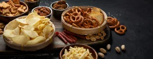 Assortment of salty snacks on dark background. Party food concept. panorama, copy space