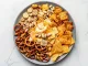 Top-down shot of party mix on a grey plate, including crackers, chips, pretzels, almonds, and pistachios. Salty snacks on a white background